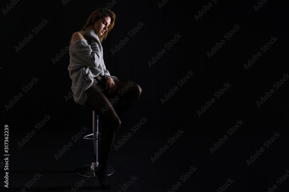 silhouette of a young beautiful girl sitting in a high chair on a dark background, low key photo, copy space