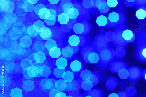 Glowing and festive blue light circles created from in camera and lens bokeh. Lights defocused giving a blurred effect. Blue background for design.
