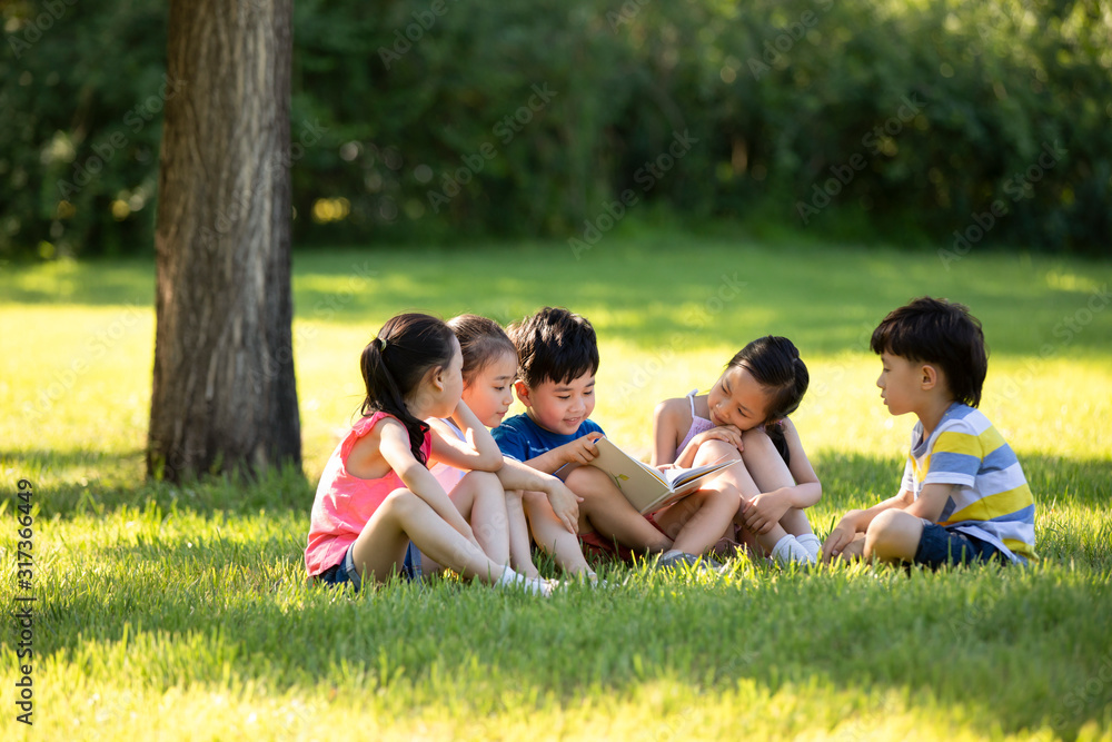 Happy children reading book on meadow Happy children reading book on meadow