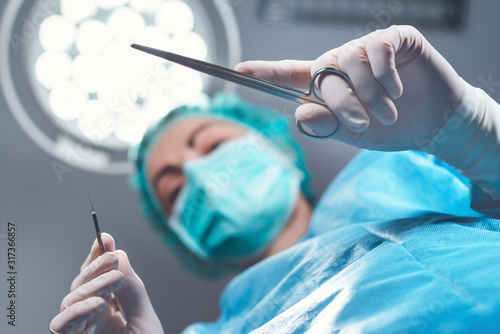 From below woman surgeon in medical uniform using professional tools while standing under bright light in operating theater photo
