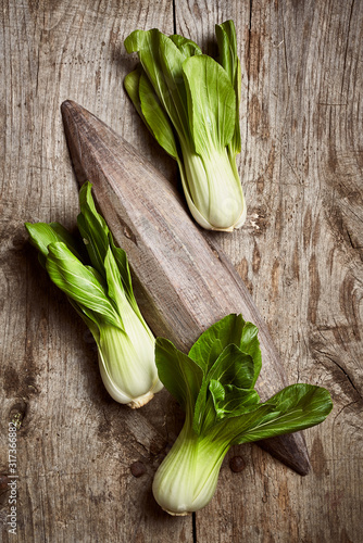 Top view of ripe bok choy placed near wooden plate on shabby lumber table in kitchen