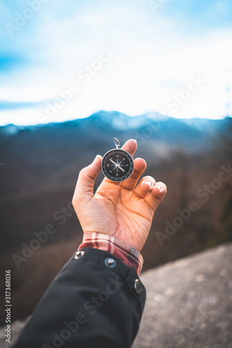 Crop person finding direction and holding compass in stretched hand in mountains photo