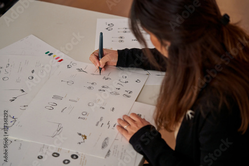 Woman sitting at a table with a pencil drawing jewels on paper