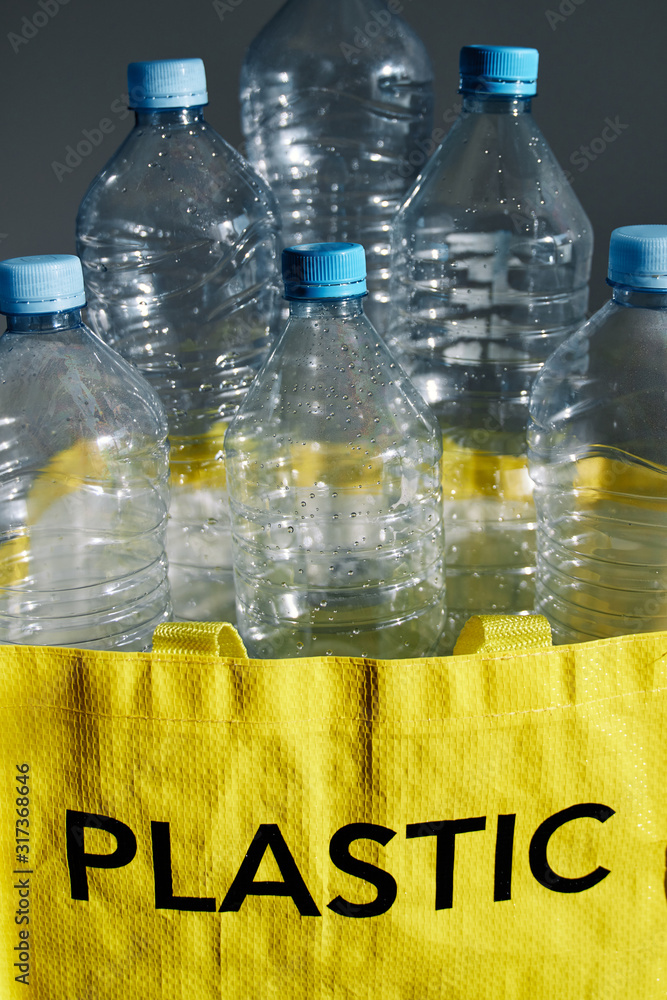 Heap of empty water bottles in yellow bag with recycle sign on gray
