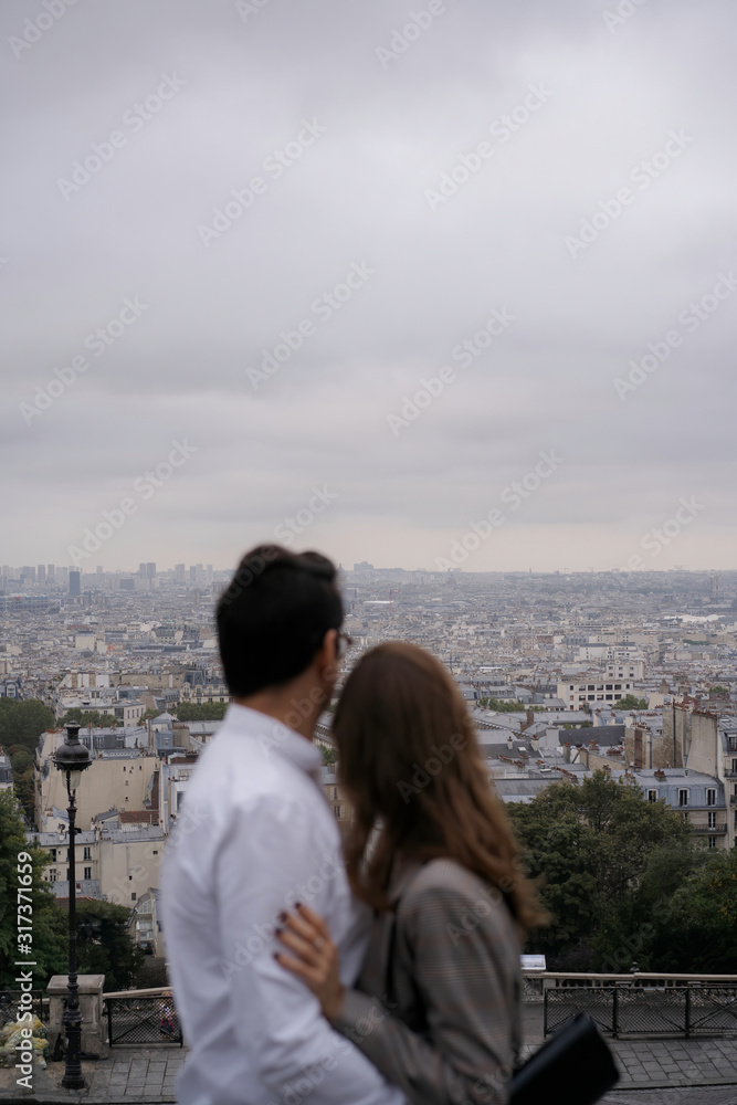 A young couple a girl and a man hug in a romantic place in Paris and admire the city from the heights of Montmartre. Honeymoon.