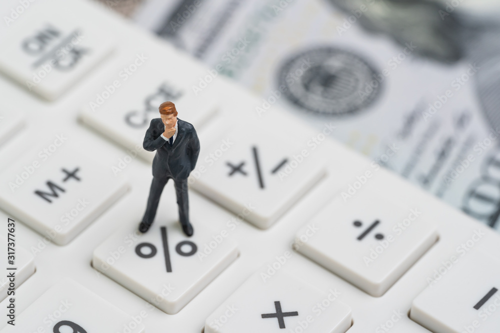 Miniature people business man standing and thinking on calculator percentage button using as FED consider interest rate, business profit or stock market analyst Miniature people business man standing and thinking on calculator percentage button using as FED consider interest rate, business profit or stock market analyst