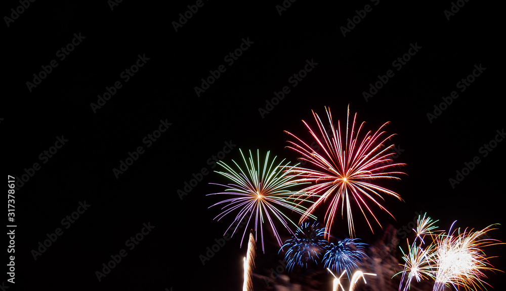 Green, red, blue, and white starburst fireworks against a black background