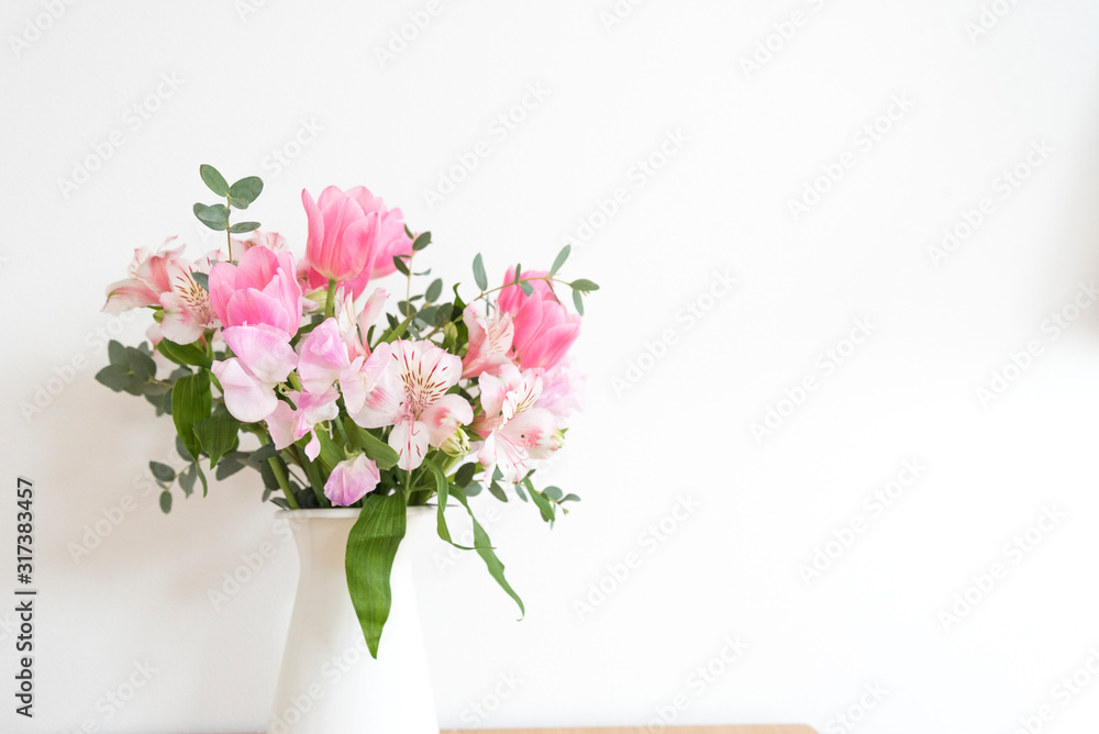 ピンク系の花とグリーン　白い壁　室内　部屋　屋内　アレンジメント　花束　花　春　ピンク　観葉植物　華やか　爽やか　春らしい　かわいい　おしゃれ　白背景　文字スペース　コピースペース　ホワイトスペース　余白　横位置