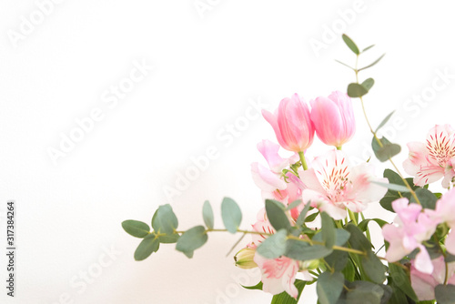 シンプルな花瓶とピンク系の花　ピンク系の花とグリーン　部屋　白壁　白背景　室内　屋内　自然光　余白　ホワイトスペース　コピースペース　文字スペース　縦　背景素材　背景　グラフィック素材　　白　緑　ピンク　春　季節　スイートピー