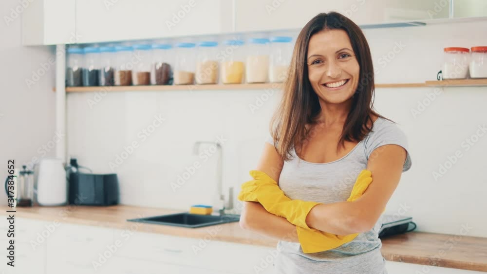 Household chores. Pretty woman, wearing yellow pubber gloves, is smiling sincerely, being in kitchen background. Copy space. Close up. 4K. Household chores. Pretty woman, wearing yellow pubber gloves, is smiling sincerely, being in kitchen background. Copy space. Close up. 4K.