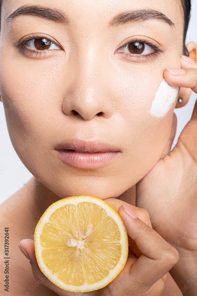 Calm young woman applying cream on facial skin Calm young woman applying cream on facial skin