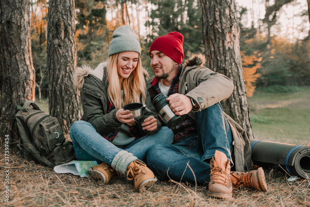 Travel couple camping with thermos having fun in the forest. Concept of trekking, adventure and seasonal vacation. Travel couple camping with thermos having fun in the forest. Concept of trekking, adventure and seasonal vacation.