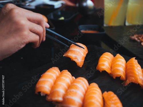 The hand is using the chopsticks to grind the salmon sushi