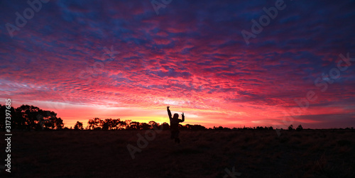 Panoramic image of vibrant pink and purple sunset sky with silhouette of small child jumping in Central Victoria, Australia