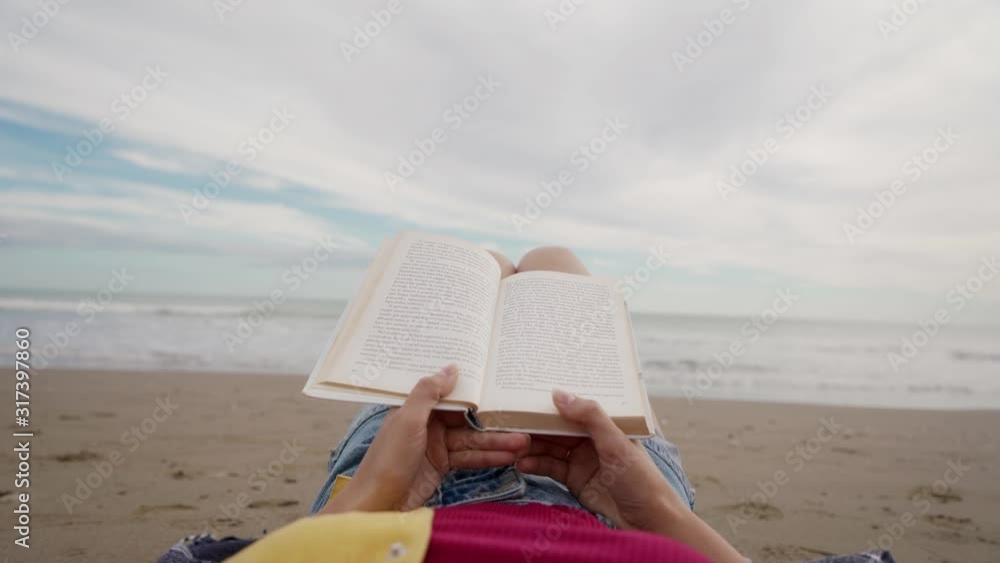 Young woman reading book lying on beach of Mediterranean Sea. Close up of book in female hands Young woman reading book lying on beach of Mediterranean Sea. Close up of book in female hands