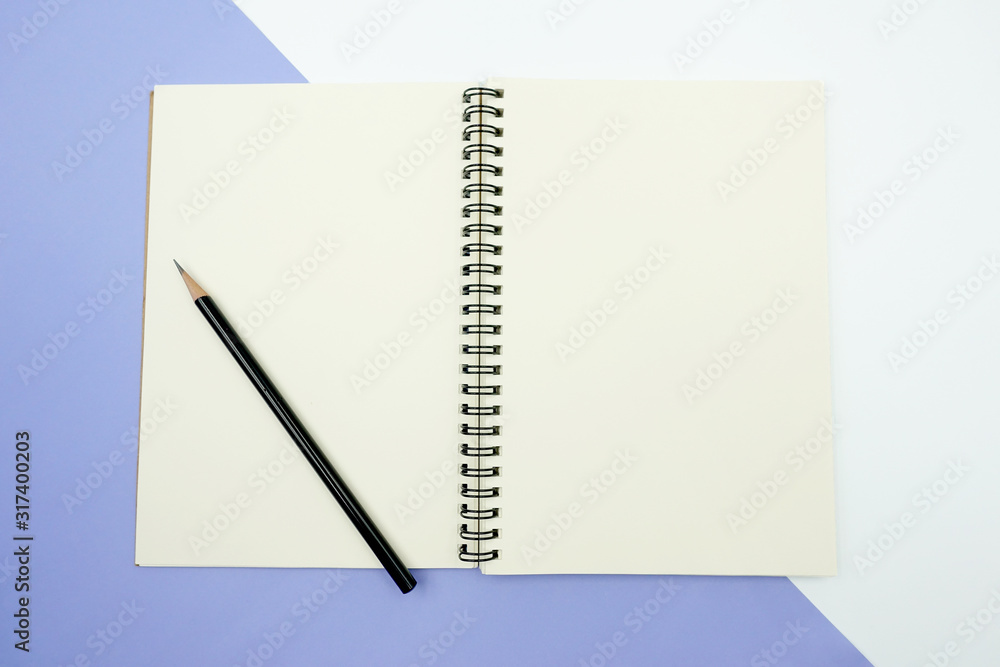 Close up top view of a blank green-read notebook paper opening and laying on two tone background of white and mauve with a black pencil on it. Close up top view of a blank green-read notebook paper opening and laying on two tone background of white and mauve with a black pencil on it.