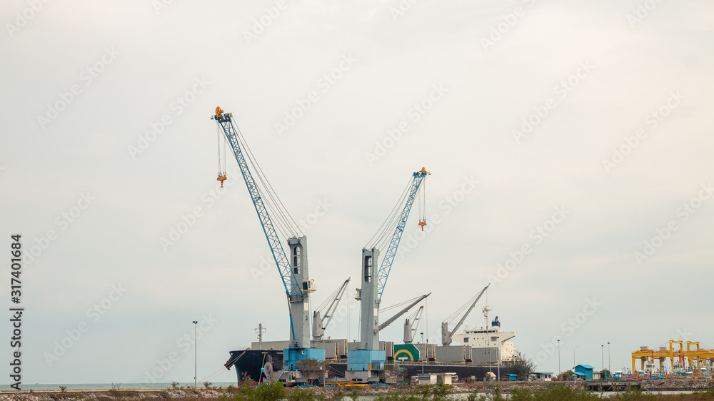 Large cargo cranes and large cargo ships dock at the harbor.