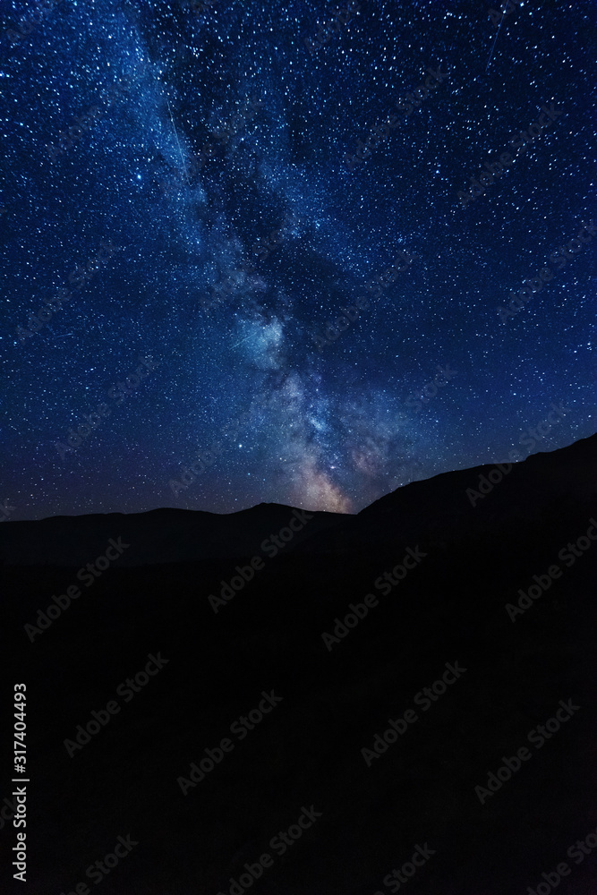 Bright starry sky with the milky way on the background of mountains and hiker with red tent.