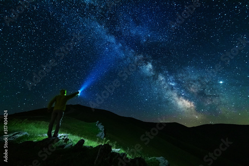 Bright starry sky with the milky way on the background of mountains and hiker with red tent.
