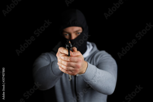 Man with a gun on a black background. The gun is in focus, the masked man is blurred.