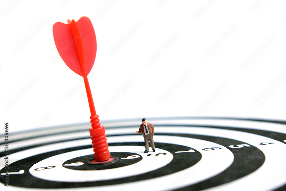 Business strategy conceptual photo - Miniature businessman pointing on red arrow on dartboard Business strategy conceptual photo - Miniature businessman pointing on red arrow on dartboard