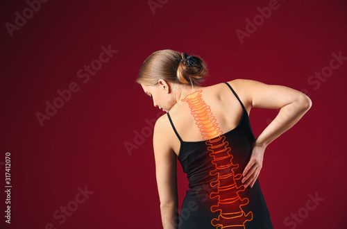 Young woman suffering from back pain on color background photo