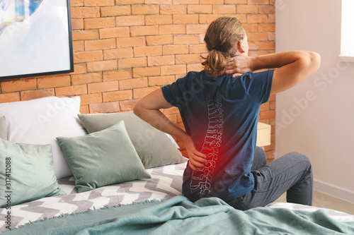 Young man suffering from back pain at home photo