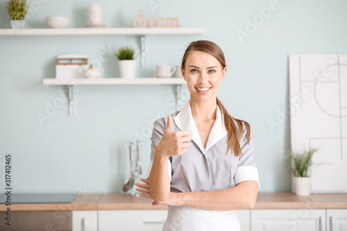 Portrait of beautiful chambermaid showing thumb-up in kitchen