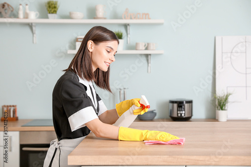 Beautiful young chambermaid cleaning kitchen