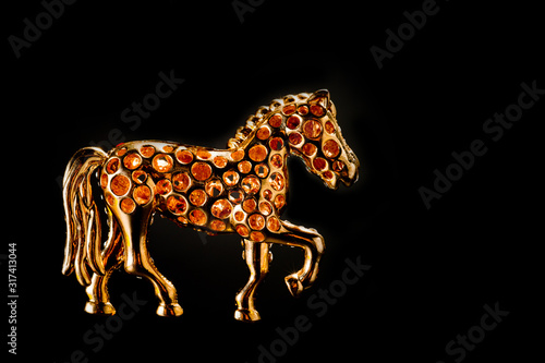 Horse figurine souvenir keychain in gold color ornate with bright pebbles shot on a dark background