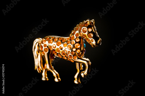 Horse figurine souvenir keychain in gold color ornate with bright pebbles shot on a dark background