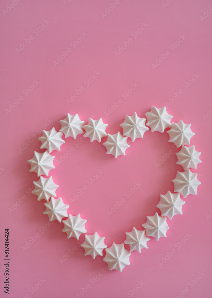 Meringue kisses in heart shape on pink background