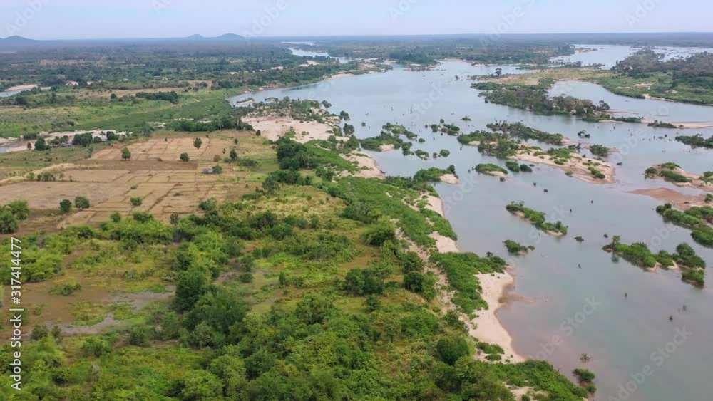 Aerial View of Mekong river affected by Spring flooding featuring Farm house, silo on dry ground, livestock, green fields, brown flood water, covered roads Aerial View of Mekong river affected by Spring flooding featuring Farm house, silo on dry ground, livestock, green fields, brown flood water, covered roads