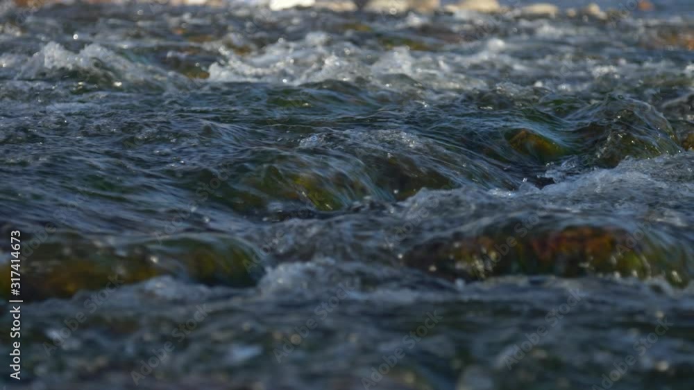 Slow tight low angle slider shot of water running over river rock during golden hour. Slow motion. Slow tight low angle slider shot of water running over river rock during golden hour. Slow motion.