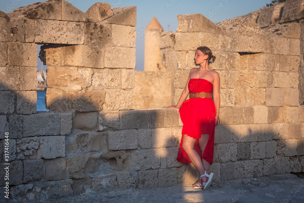 girl in a red dress is standing near an ancient stone wall girl in a red dress is standing near an ancient stone wall