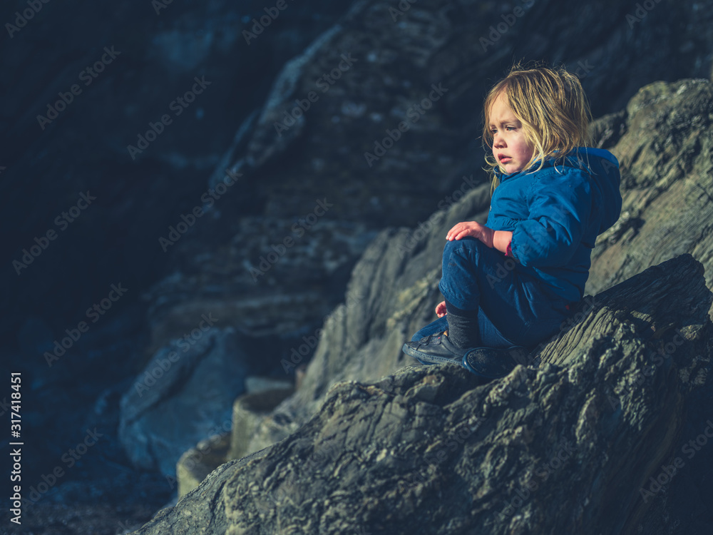 Toddler relaxing on rock in winter