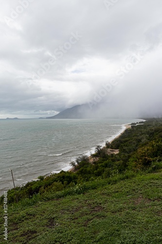 shore of the beach with fog and rain-laden clouds between the mountains in front of the beach and a lot of vegetation. Port Douglas