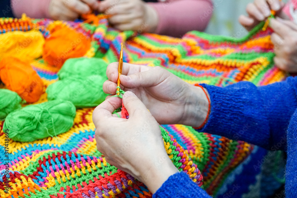 Obraz premium the hands of older women are knitted and crocheted, multi-colored woolen yarn. knitting socks, scarves and other clothes