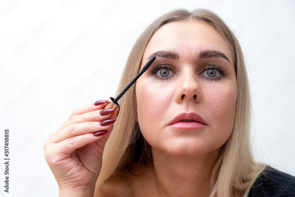 Headshot of female with bright makeup applying mascara on eyelashes. Headshot of female with bright makeup applying mascara on eyelashes.