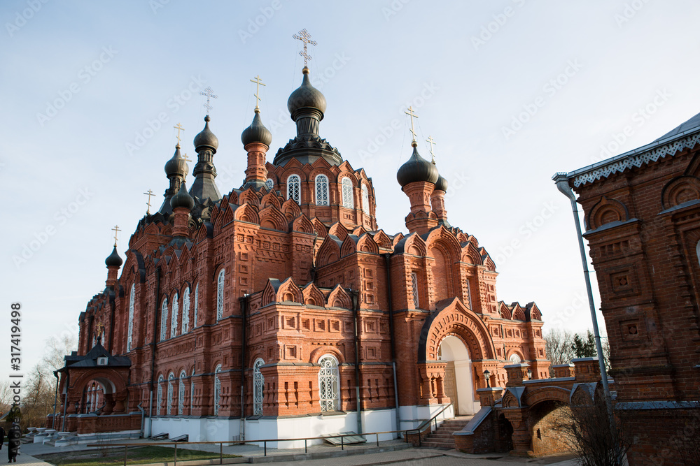 Fototapeta premium The convent of the virgin of Kaluga in the bright light of the sun. Red brick carved high walls of the monastery in Shamordino