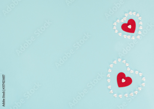 Two red felt hearts inside a hearts made of small pearl hearts on blue background. Valentine's Day, wedding, love, happiness concept. Greeting or invitation card. Flat lay style with copy space.