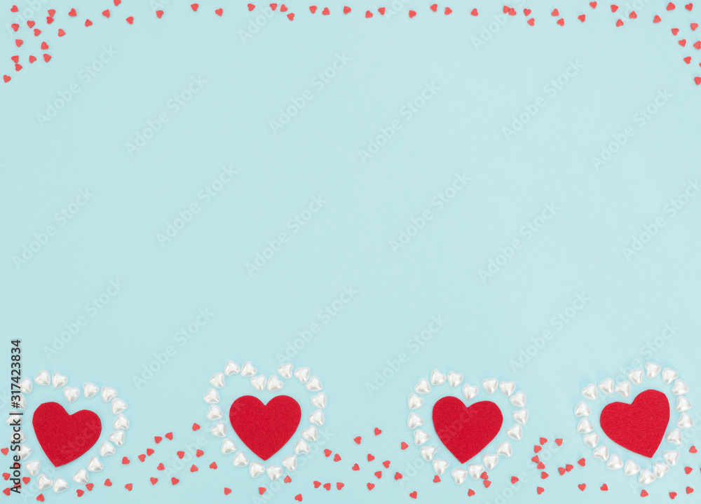 Four red felt hearts inside a hearts made of small pearl hearts on blue background. Valentine's Day, wedding, love, happiness concept. Greeting or invitation card. Flat lay style with copy space.