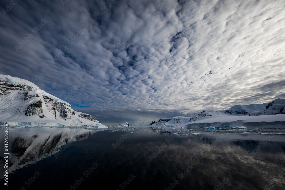 Snow and ice of the mountains reflected in the water in Antarctica, a pristine remote landscape