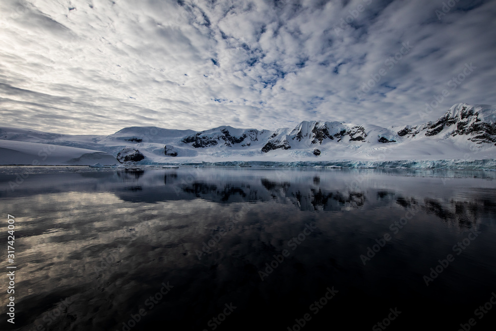 Snow and ice of the mountains reflected in the water in Antarctica, a pristine remote landscape