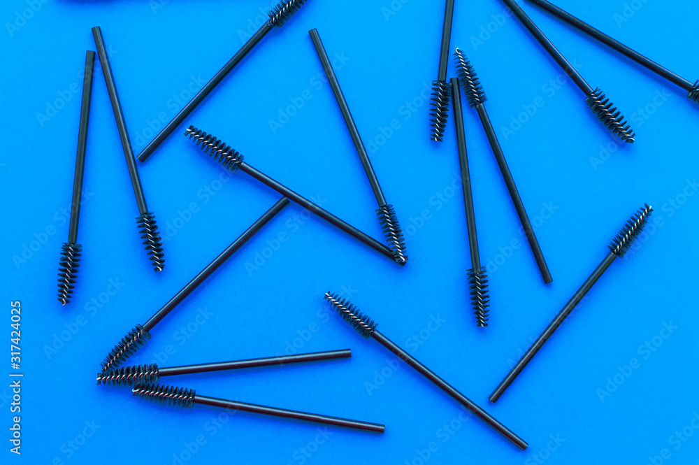 Texture. Black brushes for combing eyelashes and eyebrows are scattered on a blue background Texture. Black brushes for combing eyelashes and eyebrows are scattered on a blue background