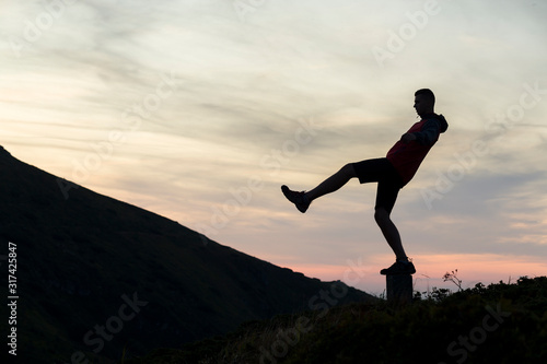 Wallpaper Mural Dark silhouette of a hiker balancing on a summit stone in evening mountains. Torontodigital.ca