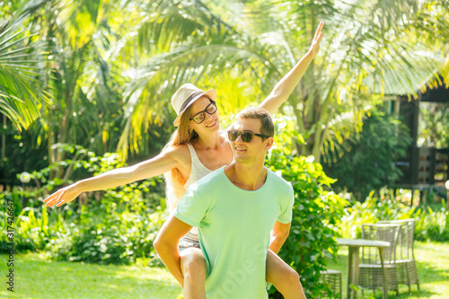 Young loving couple hugging and play airplane fly under palms in deck chair lounge resor doing piggyback