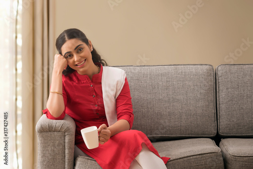Obraz na płótnie Happy single woman sitting on the sofa at home with a cup of coffee in hand