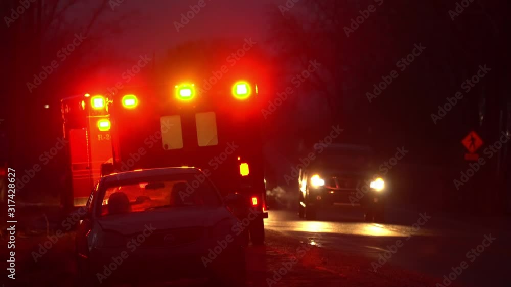 Flashing lights of emergency vehicles on side of roadway as cars slowly drive by. Flashing lights of emergency vehicles on side of roadway as cars slowly drive by.