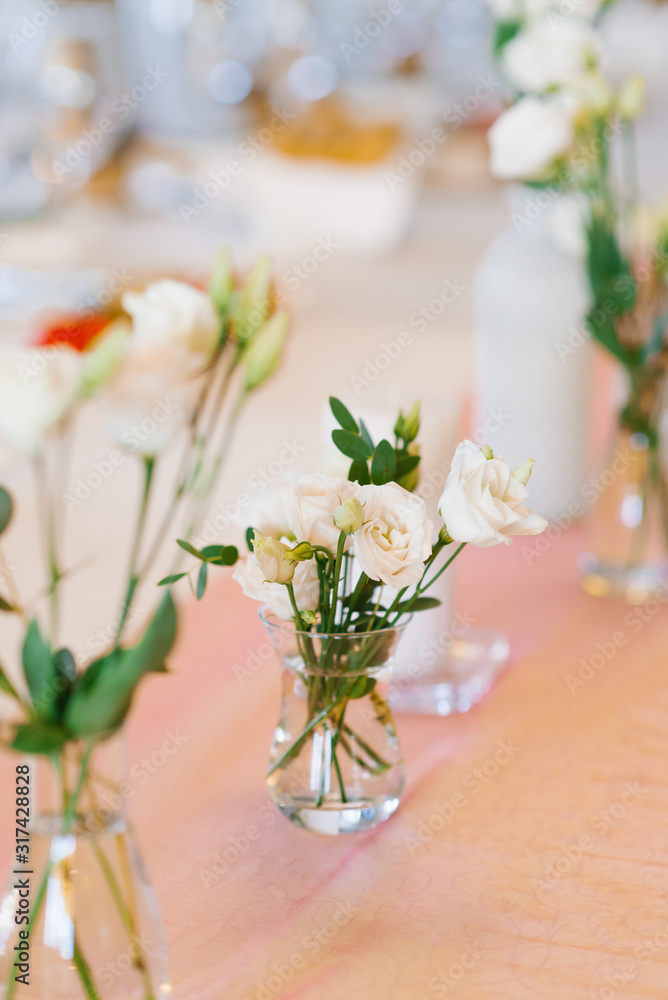 White eustoma flowers in a glass vase stands on a table. Wedding banquet table